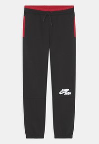 Schwarze Jogginghose mit roten Seitenelementen. Sie verfügt über einen elastischen Bund, eine verstellbare Kordel und ein weißes "Jumpman"-Logo am linken Bein.