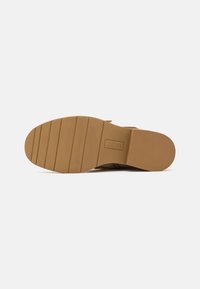 Sola de borracha castanha com ranhuras horizontais e uma superfície texturada. Salto quadrado e logo estampado num painel lateral. Design limpo e minimalista.