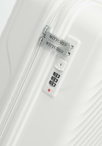 Maleta blanca de concha dura con un diseño texturizado, cierre de cremallera y una cerradura de combinación con tres diales. Etiquetas de la marca visibles.