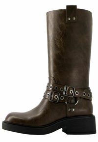 Hnědé kožené holínky až po kolena s kulatou špičkou, černou podešví a cvočkovými pásky. Mají texturovaný povrch a postranní poutko pro snadné nazouv�ání.