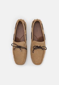 Hellbraune Mokassins mit strukturiertem Finish, braunen Schnürsenkeln, kontrastierenden Nähten und weichem Innenfutter. Im Slipper-Stil gestaltet.