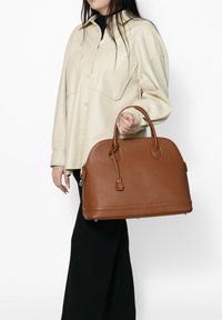 Borsa a mano in pelle marrone con parte superiore arrotondata, chiusura a zip e due manici. Finitura testurizzata con un accento di portachiavi e piedini protettivi alla base.