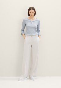 Camiseta henley azul claro de manga larga, combinada con pantalones anchos color crema. Zapatillas blancas completan el atuendo. Diseño sencillo y ajuste relajado.