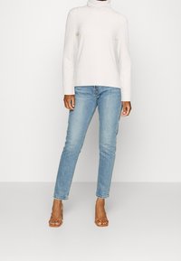 Top blanco de cuello alto con relieve, jeans rectos de mezclilla azul claro y sandalias marrones de tiras. Diseño simple, textura suave y corte relajado.