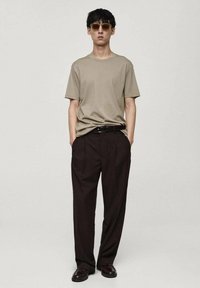 T-shirt beige in cotone abbinato a pantaloni a pieghe marrone scuro, indossato con una cintura nera e occhiali da sole marroni; texture liscia, vestibilità rilassata.