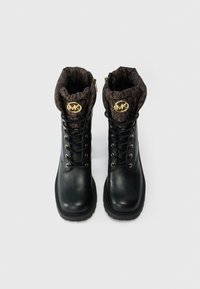 Botas de tornozelo em pele preta com acessórios dourados, apresentando um punho padrão castanho e um design de atacadores na frente. Sola robusta em borracha para melhor tração.