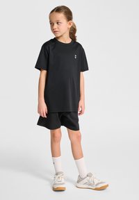 T-shirt noir à manches courtes avec un petit logo blanc, associé à un short noir, des chaussettes blanches et des baskets grises avec des semelles en gomme.
