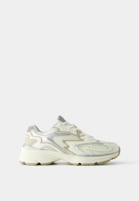 The shoe features a white mesh material with silver accents, textured design elements, and a thick, beige sole for support.