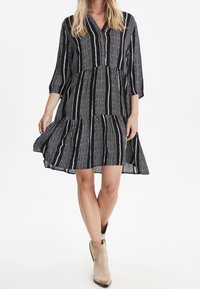 Musta-valkoinen raitamekko kerrostetulla helmalla, V-pääntiellä ja kolmannelta neljännekseltä hihoilla. Kankaan pinnassa on teksturoitu kuvio.