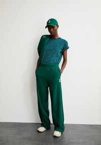Green jogger pants with elastic waistband and side pockets, paired with a striped blue and green t-shirt. Includes a matching cap.
