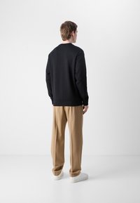 Zwarte sweatshirt met een ronde hals, gecombineerd met beige losse broeken. Witte sneakers maken de outfit af. Eenvoudig en modern ontwerp.