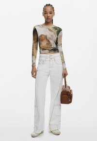 Langemouwen top met een kleurrijke abstracte print, gecombineerd met witte jeans met zichtbare stiksels en zakken, aangevuld met een bruine tas.
