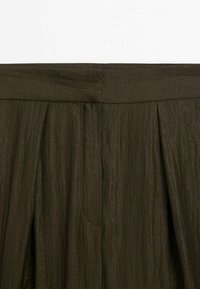 Jupe plissée vert foncé avec une surface texturée et une ceinture sans couture. Dispose d'une poche latérale pour plus de fonctionnalité.