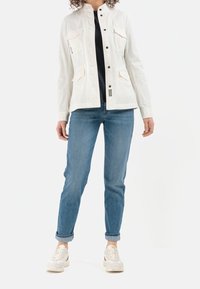 Biała bawełniana kurtka z dwoma przednimi kieszeniami, czarnymi napami i stójką. Połączona z niebieskimi dżinsami i białymi trampkami.