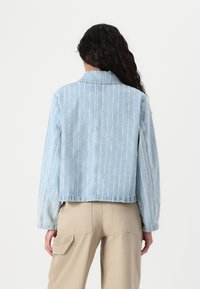 Kerge helesinine denim-jakk vertikaalsete valgete triipudega, klassikalise kraega, pikkade varrukatega ja tooriku servaga.