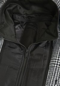 Innenansicht einer schwarzen Reißverschlussjacke mit glatter Oberfläche und weicher, gepolsterter Fütterung. Der Kragen ist teilweise geöffnet und zeigt das Innendesign.