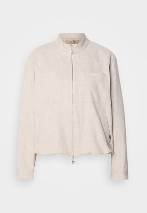 Lys beige jakke med høj krave, frontlynlås, to brystlommer og en tekstureret overflade. Croppet design og diskrete sømdetaljer.