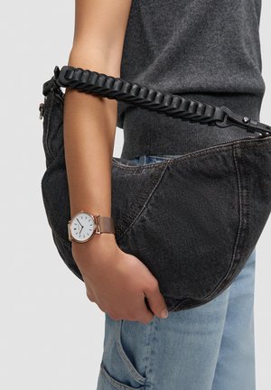 Sac en denim noir avec une sangle noire tressée, accompagné d'une montre-bracelet en maille argentée et or rose, avec un cadran blanc et un design minimaliste.