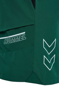 Shorts sportivi verdi con un logo bianco "HUMMEL" e motivi a chevron. Il tessuto è liscio con una leggera lucentezza e include una tasca.
