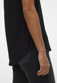 Black short-sleeve top with a lightweight fabric, featuring a curved hem and a relaxed fit, paired with dark denim jeans.