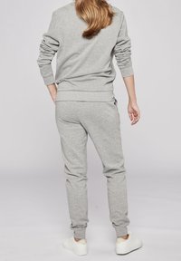 Gray sweat set featuring a long-sleeve top and tapered pants, both in a soft material with ribbed cuffs. White sneakers complete the look.