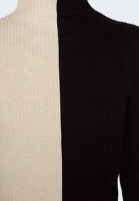 Rippstrick-Turtleneck-Pullover mit einem geteilten Design, wobei eine Seite beige und die andere Seite schwarz ist. Weicher Stoff mit kontrastierenden Farben.