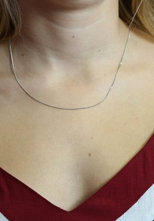 Zilveren ketting met een glad, dun en flexibel ontwerp, dat rond de hals op blote huid rust.