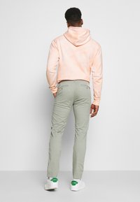 Peach tie-dye hoodie with a kangaroo pocket, paired with light green tapered pants and white sneakers with green accents.