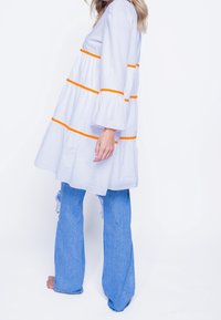 Bílé šaty s oranžovými pruhy, s širokými rukávy do zvonku, vrstvený design, doplněné světle modrými zvonovými džíny s distressed akcenty.