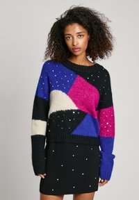 Bunt gestrickter Pullover mit schwarzen, blauen, rosa und beigen Patches, versehen mit strukturiertem Garn und silbernen Perlenakzenten. Lockere Passform mit langen Ärmeln.