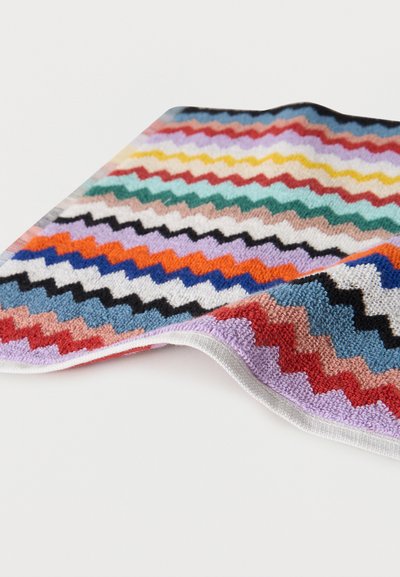 Πολύχρωμη πετσέτα υφασμένη με ζιγκ ζαγκ μοτίβο, με υφή πλεκτού, ελαφρώς διπλωμένη πάνω σε λευκή επιφάνεια.