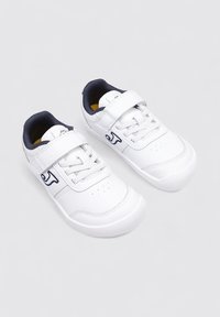 Zapatillas deportivas blancas con parte superior sintética lisa, correa de velcro y detalles en color marino. Perforaciones en la puntera para transpirabilidad. Suela de goma.