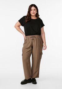 Černé tričko s krátkým rukávem spárované se světle hnědými cargo kalhotami s elastickým pasem a kapsami. Černé platformové boty dotvářejí celý outfit.