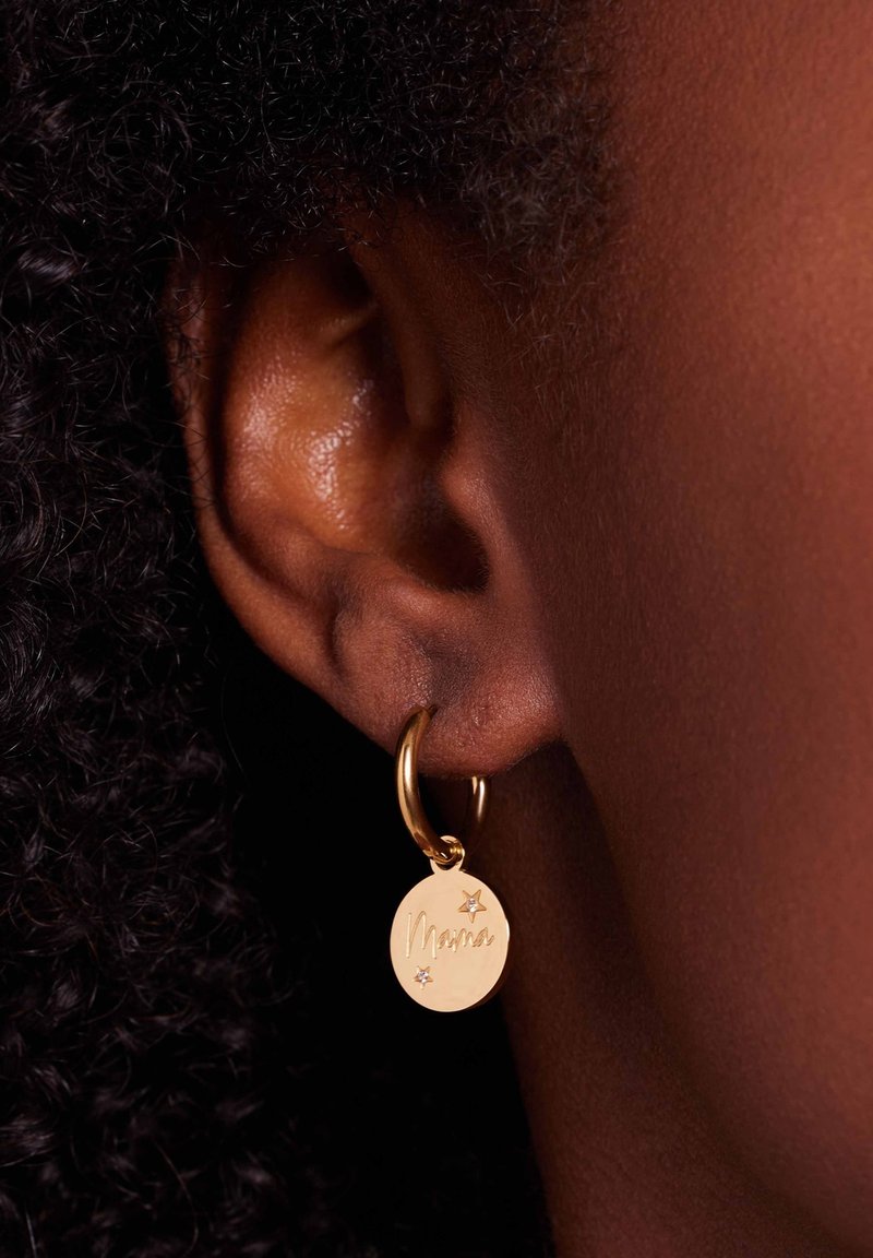 Boucle d'oreille en or avec un charme circulaire. Le charme présente un texte gravé "Mama" et deux accents en forme d'étoile. Fini lisse et poli.