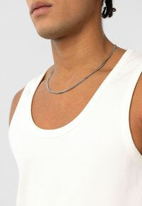 Witte geribde tanktop met een ronde halslijn, gedragen met een zilveren ketting. De stof lijkt glad en aansluitend.