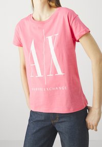 Różowa bawełniana koszulka z okrągłym dekoltem i krótkimi rękawami, z białym nadrukiem "AX" oraz napisem "ARMANI EXCHANGE" z przodu.
