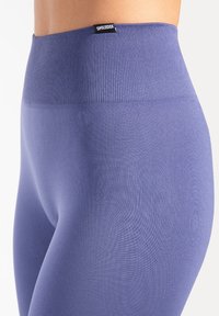 Leggings taille haute violets en tissu extensible avec une ceinture côtelée et une texture lisse, ornés d'une étiquette logo en haut.