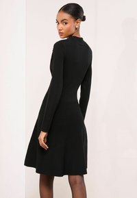 Rochie neagră cu mânecă lungă, cu un corset fixat și fustă evazată. Textură netedă, design simplu, prezintă un detaliu subtil la decolteu.