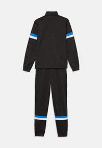 Chándal negro con chaqueta de cremallera y pantalones con cinturilla elástica. La chaqueta tiene rayas horizontales azules y blancas en las mangas.