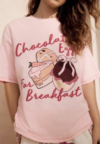 Růžové tričko s krátkým rukávem s ilustracemi dezertů: cupcakes, čokoládového vejce a dortu s textem "Čokoládová vejce na snídani."