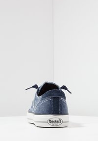 Denim low-top sneaker in dark blue features white stitching, logo on heel, and tonal laces with textured fabric and a rubber sole.