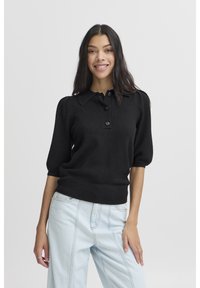 Juodas trumpomis rankov�ėmis polo megztinis su ribbinguotu apačia, sagų užsegimu ir minkšta tekstūra, derinamas su šviesiais džinsiniais kelnėmis.