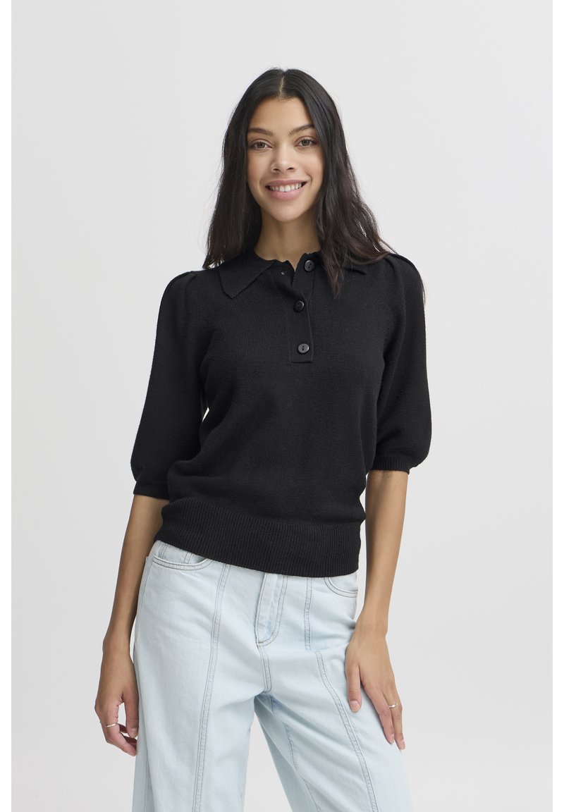 Juodas trumpomis rankovėmis polo megztinis su ribbinguotu apačia, sagų užsegimu ir minkšta tekstūra, derinamas su šviesiais džinsiniais kelnėmis.