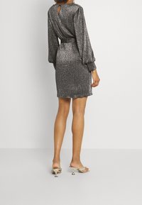 Glittrig grå klänning med långa puffärmar, åtsitsande midja och nyckelhållsdetalj bak. Stylad med metalliska högklackade sandaler.