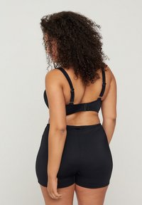 Zwarte bh met verstelbare bandjes, haaksluiting op de rug, gecombineerd met zwarte shorts. Glad materiaal en aansluitend ontwerp.