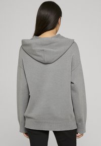 Sweat à capuche gris à coupe ample, ourlet côtelé et manches larges. Le tissu semble doux avec une texture lisse et des détails de couture subtils.