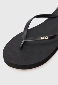 Schwarze Flip-Flops mit strukturierten Sohlen, dünnen matten Riemen und einem metallic-goldenen Logo-Akzent. Entworfen für Komfort und lässiges Tragen.