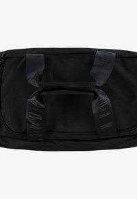 Bolsa de deporte de tela negra con cierre de cremallera. Presenta asas acolchadas y correas con logotipo texturizado. Superficie suave sin patrones visibles.