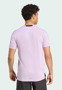 Camiseta deportiva de color púrpura claro hecha de un material suave, con mangas cortas, un cuello redondo y un pequeño acento negro en la parte trasera.