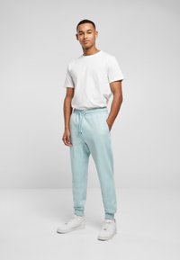 Lyseblå bomullsjoggers med elastisk midje og snøring, sammen med en enkel hvit t-skjorte med rund hals og hvite joggesko.
